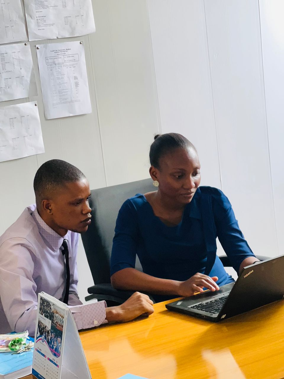 Ifeoluwa Bodunde, Rising Scholars online course participant's photo. 2 people sit at a desk, both looking like they'e concentrating looking at something on an open laptop on the desk in front of them